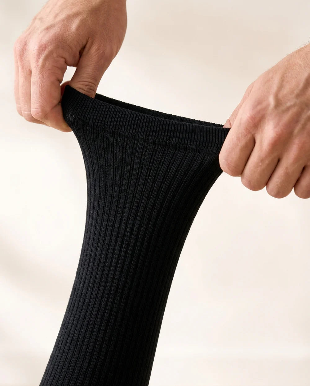 Two hands stretching the ribbed top cuff of the black compression sock wide open — the stretch test